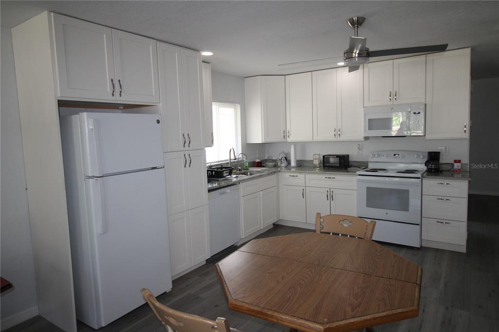 A kitchen with white cabinets, white appliances, and a wooden table in the foreground — 812 OLEANDER AVENUE, HOLLY HILL, FL
