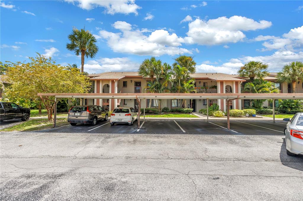 A two-story apartment building features a covered parking area with several parked cars — 723 83RD AVENUE N UNIT 102, ST PETERSBURG, FL