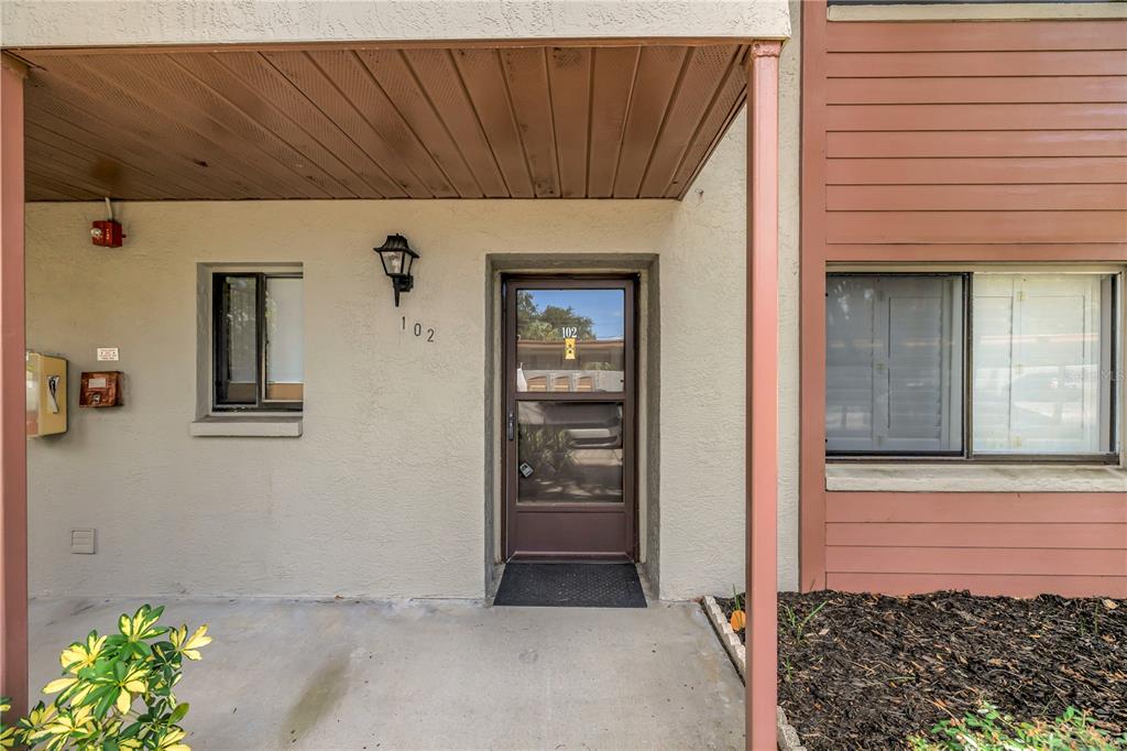 The exterior entrance of a ground-floor apartment features a screen door and a small porch — 723 83RD AVENUE N UNIT 102, ST PETERSBURG, FL