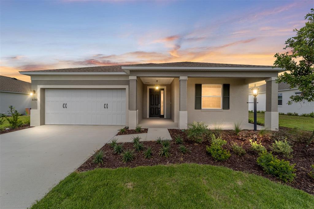 A single-story house with a two-car garage, covered entryway, and landscaped front yard at sunset — 10352 SW 107TH COURT, OCALA, FL