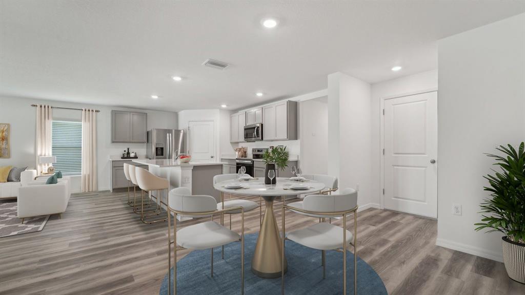 A modern open-concept kitchen and dining area with light wood flooring and gray cabinetry — 3512 HARVEST GARDENS LOOP, PLANT CITY, FL