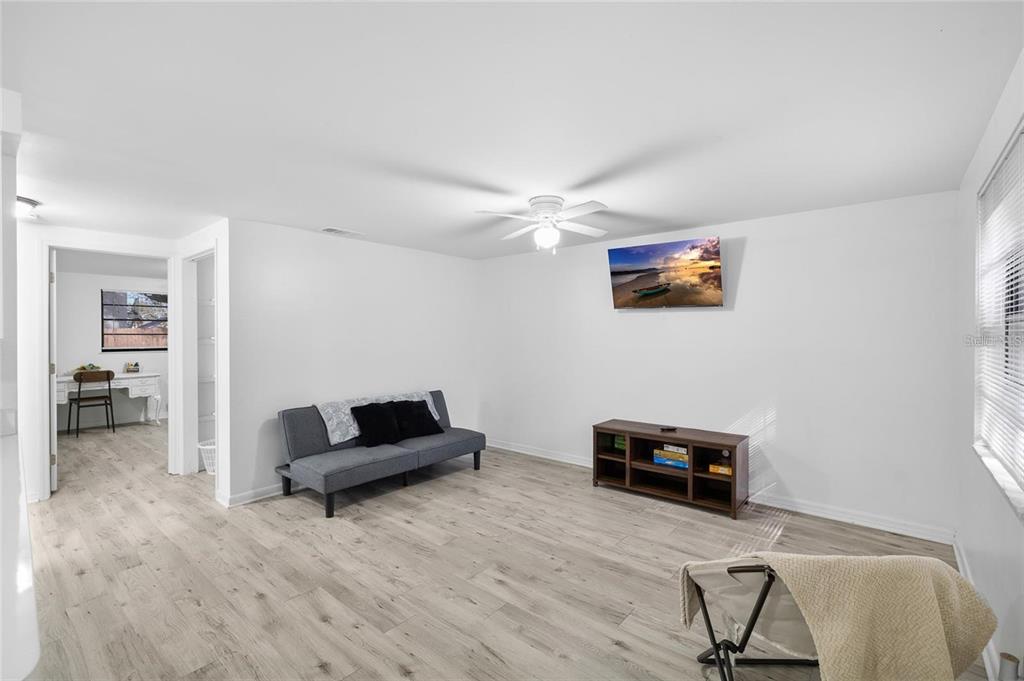 A living room with light wood-look flooring, a gray futon, and a wall-mounted television — 1220 E 142ND AVENUE UNIT A, TAMPA, FL