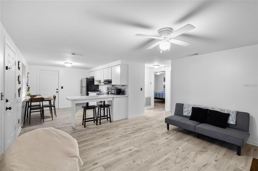 An open-concept living room and kitchen with white cabinets, wood-look flooring, and a gray sofa — 1220 E 142ND AVENUE UNIT A, TAMPA, FL
