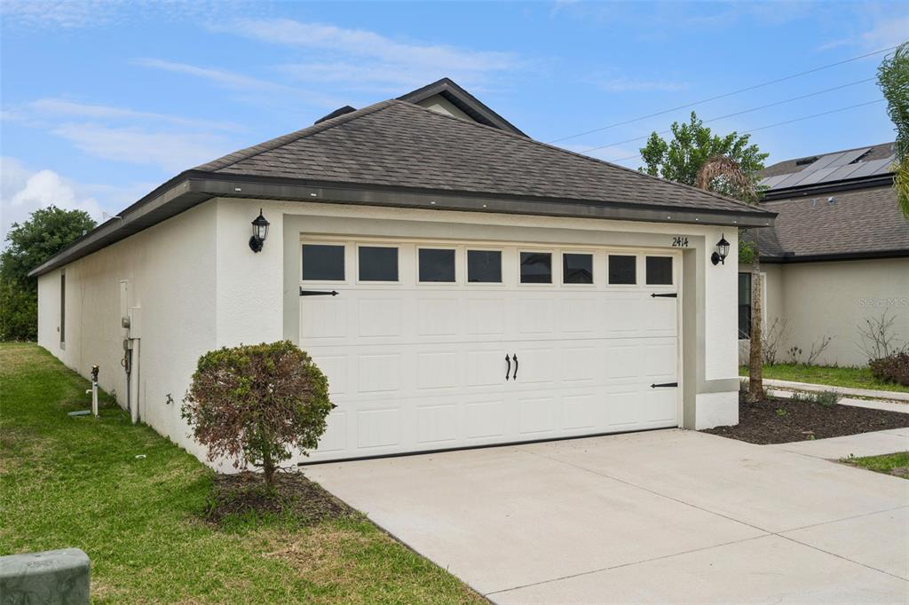 A white garage with a tan trim and a shingled roof faces a concrete driveway — 2414 CASPIAN DRIVE, LAKELAND, FL