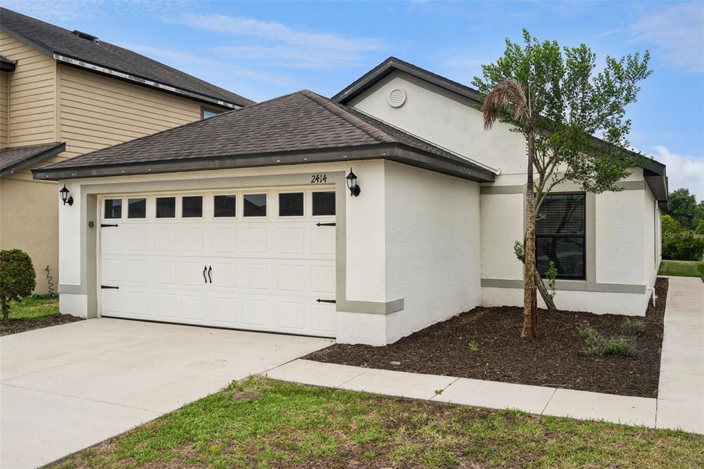 A single-story house with a white stucco exterior, a two-car garage, and a small palm tree — 2414 CASPIAN DRIVE, LAKELAND, FL