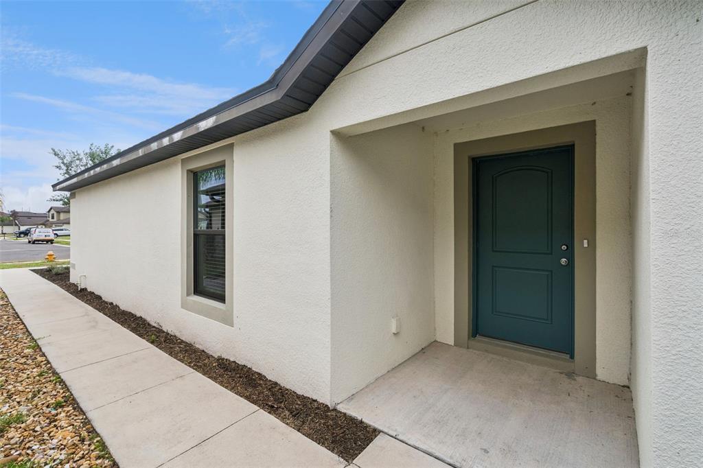 A white stucco house exterior features a dark teal front door and a concrete walkway — 2414 CASPIAN DRIVE, LAKELAND, FL