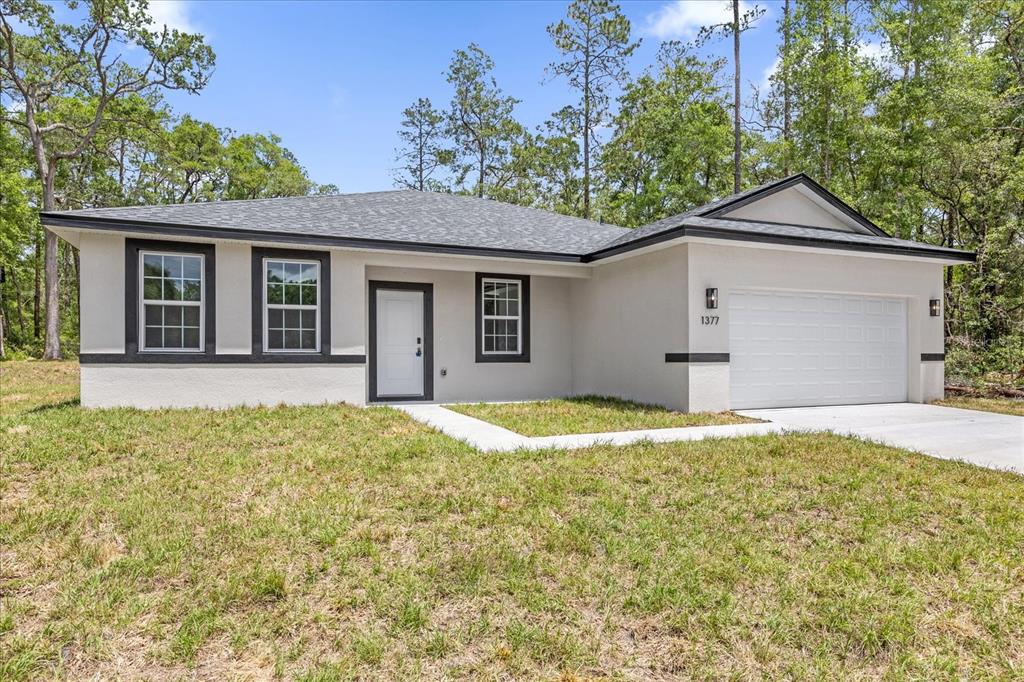 A single-story house with a white stucco exterior, dark trim, and a two-car garage — 1377 W ALEXANDER DRIVE, CITRUS SPRINGS, FL