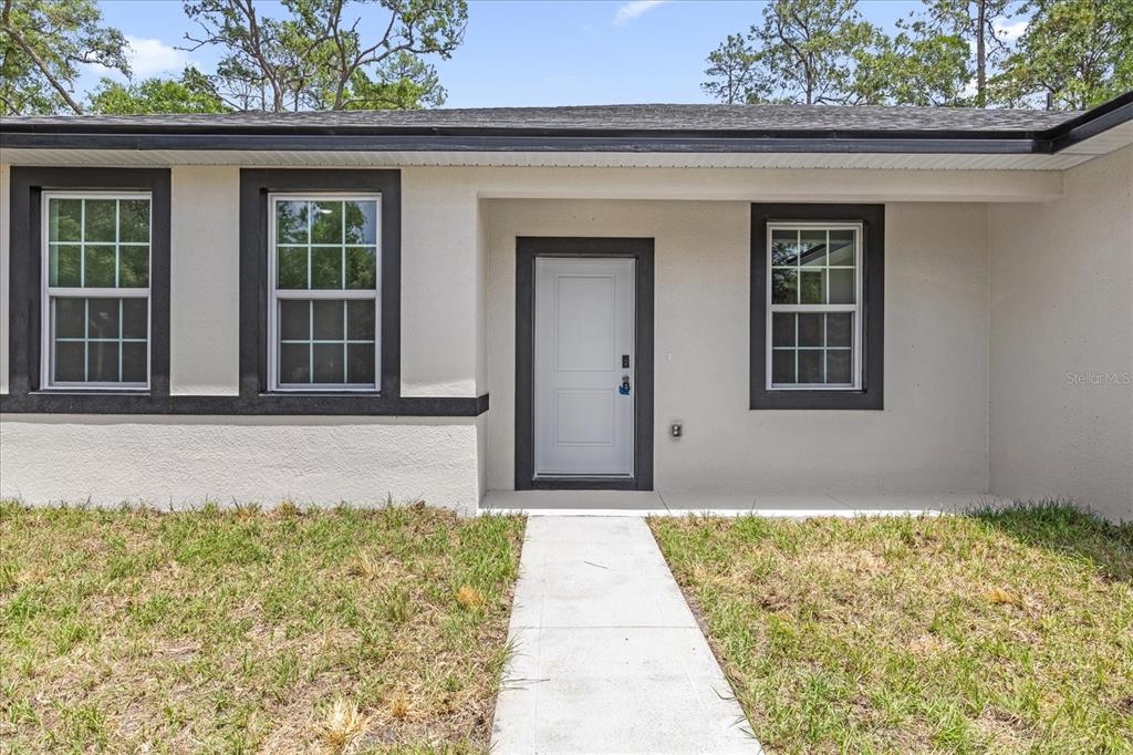 The exterior of a single-story house features a white door, dark trim, and concrete walkway — 1377 W ALEXANDER DRIVE, CITRUS SPRINGS, FL