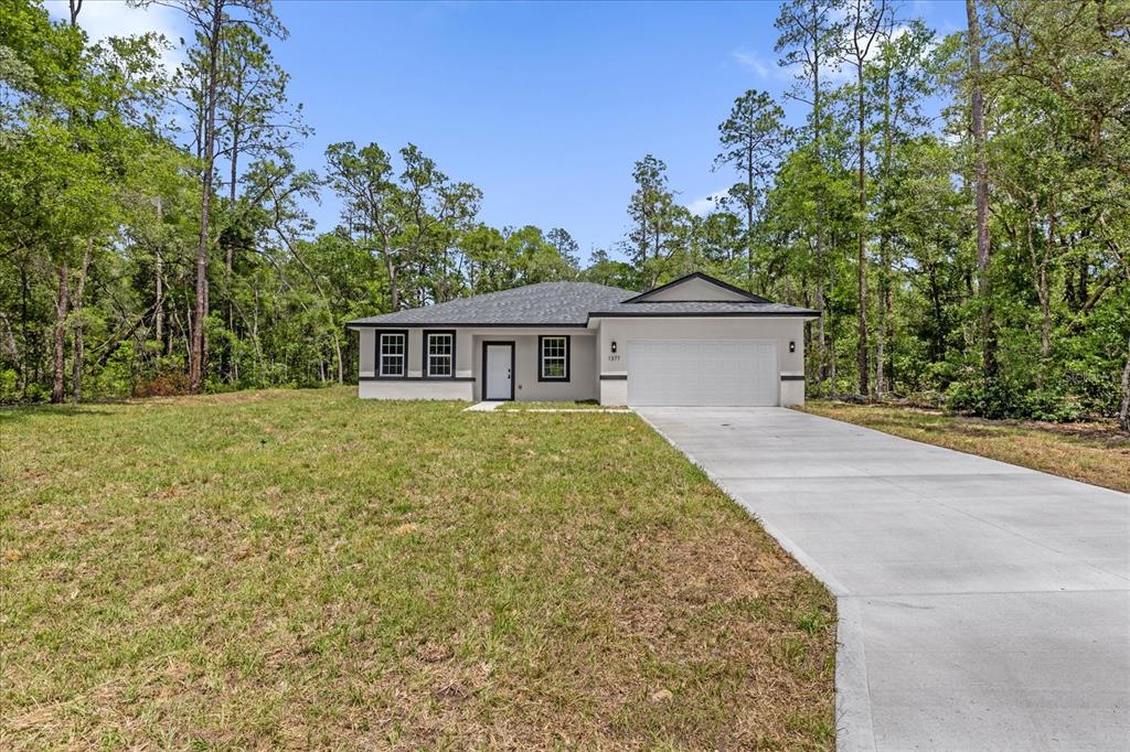 A single-story house with a white exterior, dark roof, and concrete driveway sits among trees — 1377 W ALEXANDER DRIVE, CITRUS SPRINGS, FL
