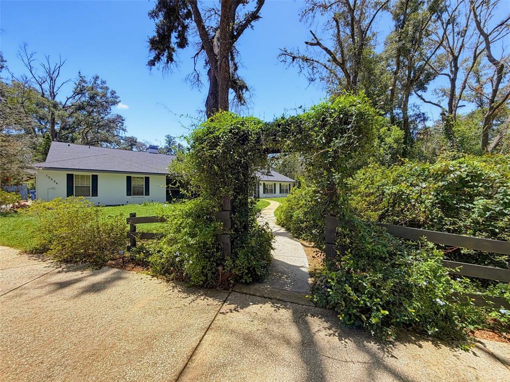 A stone path leads through a vine-covered wooden arbor toward a white house — 15234 SCANIO, SPRING HILL, FL