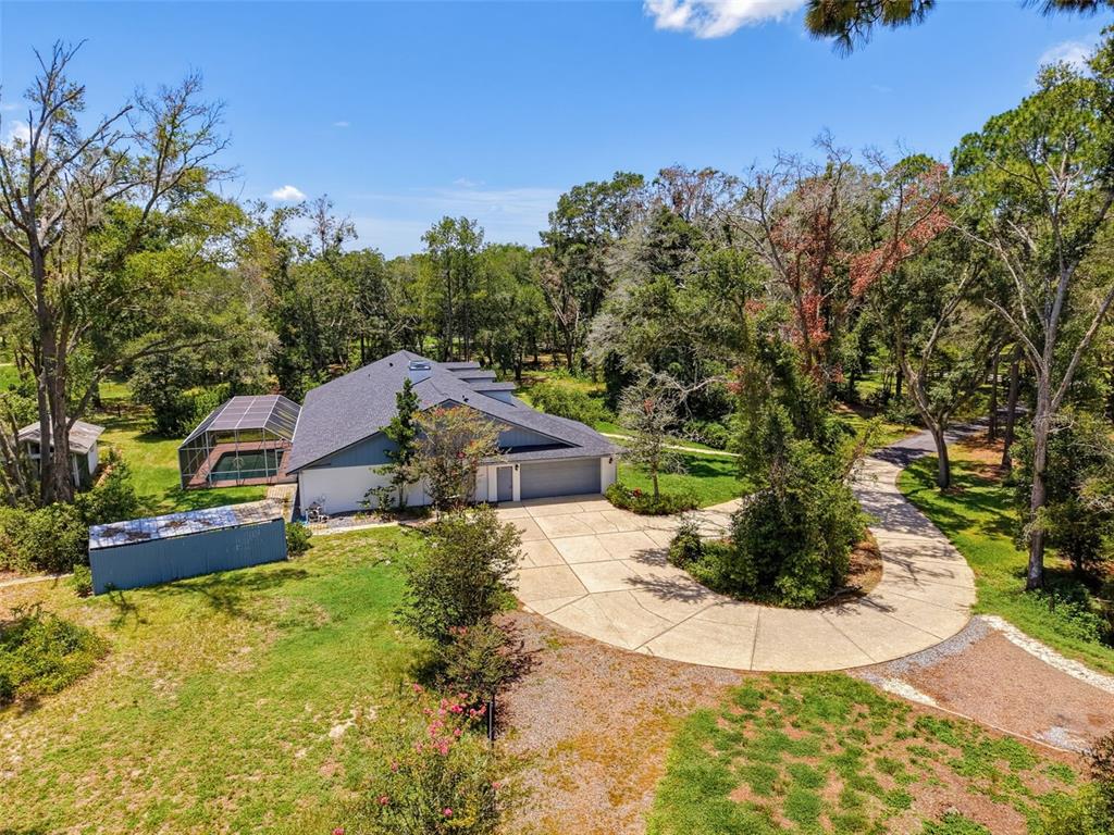 An aerial view shows a house with a pool enclosure, a circular driveway, and trees — 15234 SCANIO, SPRING HILL, FL