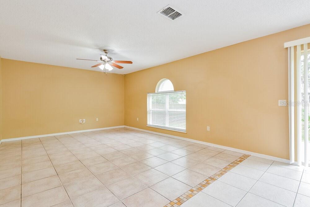 An empty living room features beige walls, light-colored tile flooring, and a ceiling fan — 2047 GALAHAD DRIVE, DELTONA, FL
