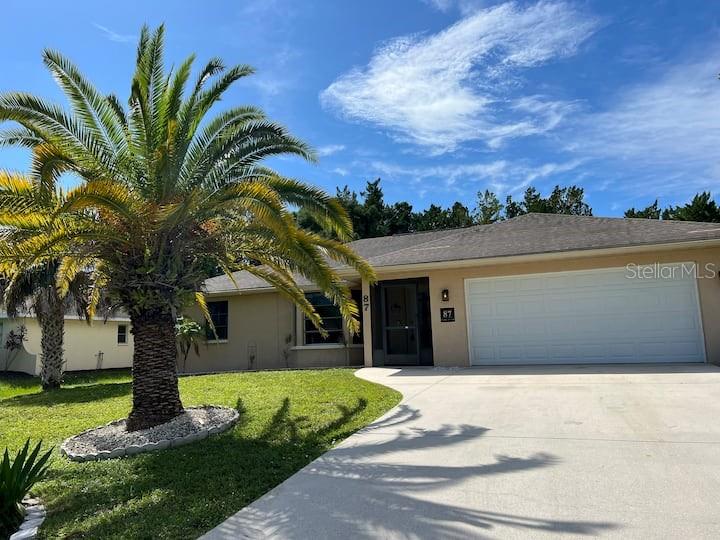 A single-story house with a large palm tree in the front yard and a garage — 87 MARK TWAIN LANE, ROTONDA WEST, FL