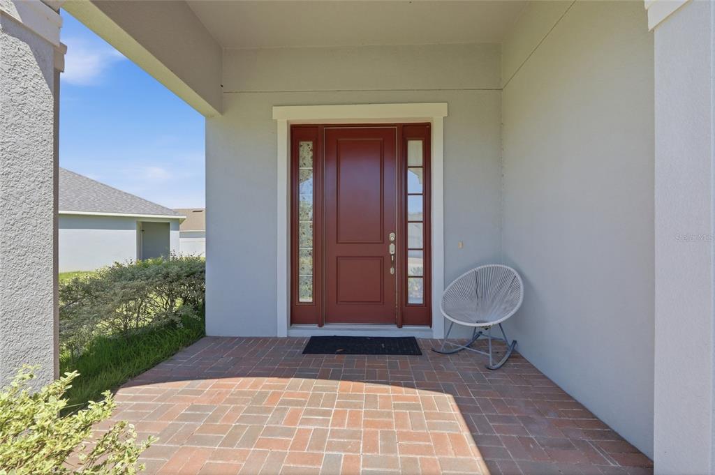 A red front door with sidelights sits on a brick porch with a rocking chair — 2252 RUSH BAY WAY, ORLANDO, FL