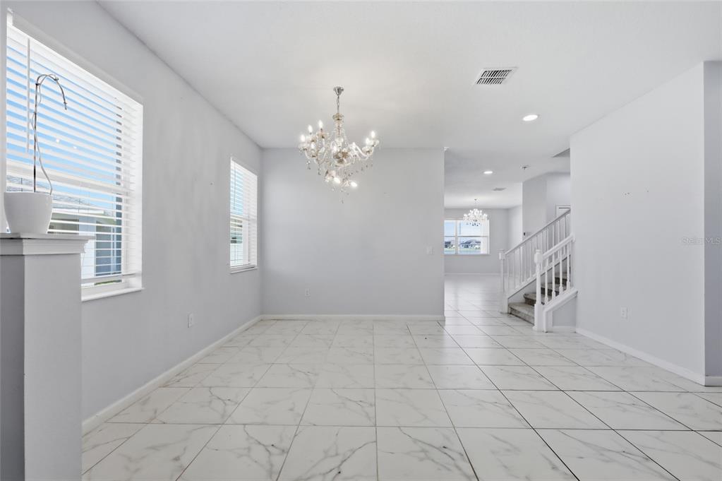 A bright dining room features white marble-look tile floors, a crystal chandelier, and a staircase — 2252 RUSH BAY WAY, ORLANDO, FL
