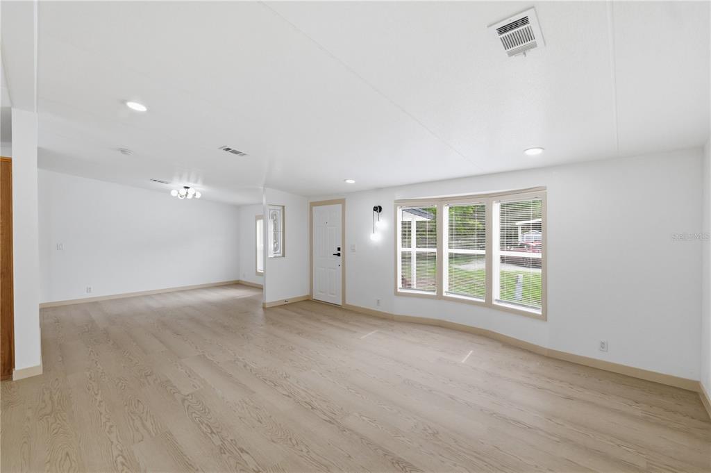 A bright, empty living room features light wood-look flooring, white walls, and a bay window — 8726 N MEADOWVIEW CIR, TAMPA, FL