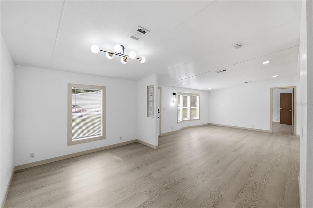 A bright, empty living room features light wood-look flooring, white walls, and a modern chandelier — 8726 N MEADOWVIEW CIR, TAMPA, FL