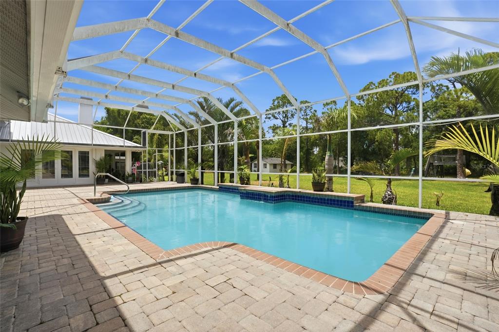 A swimming pool with a screened enclosure and paver patio sits behind a residential home — 23494 WESTCHESTER BOULEVARD, PUNTA GORDA, FL