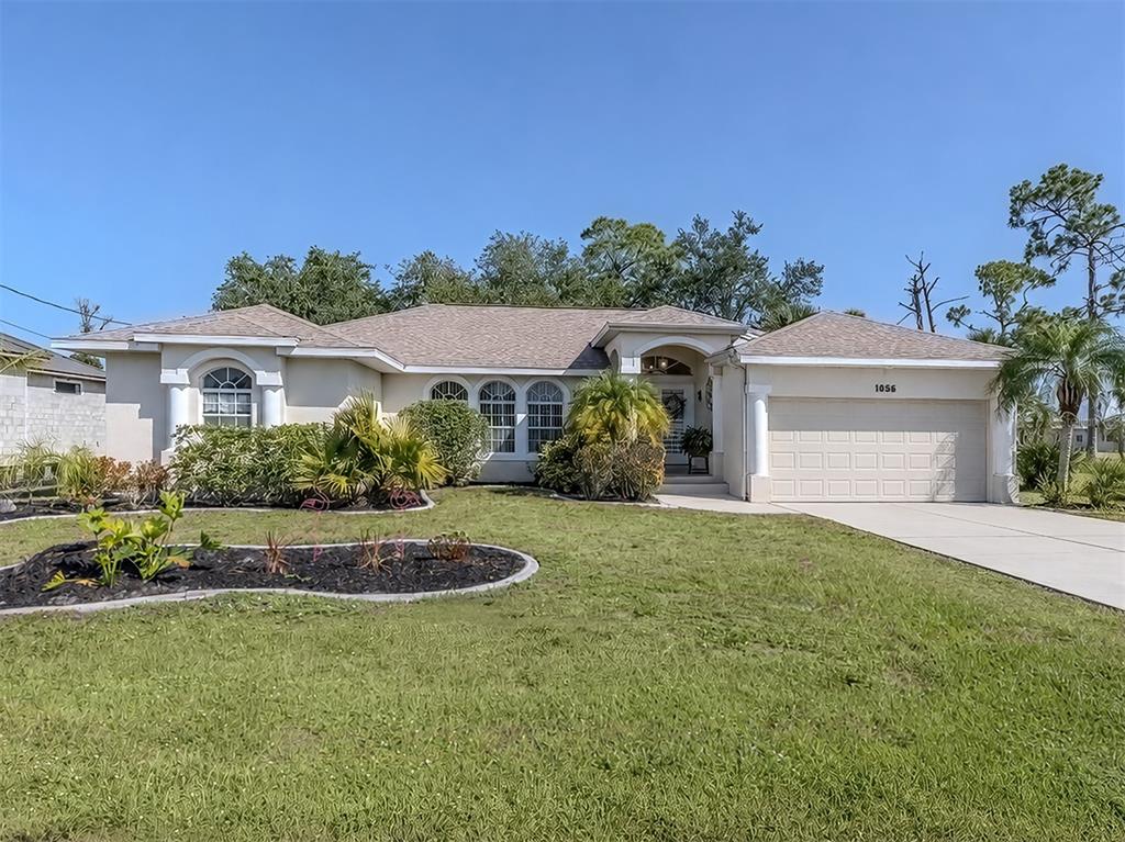 A single-story house with a beige stucco exterior, a two-car garage, and landscaped front yard — 1056 ROTONDA CIRCLE, ROTONDA WEST, FL