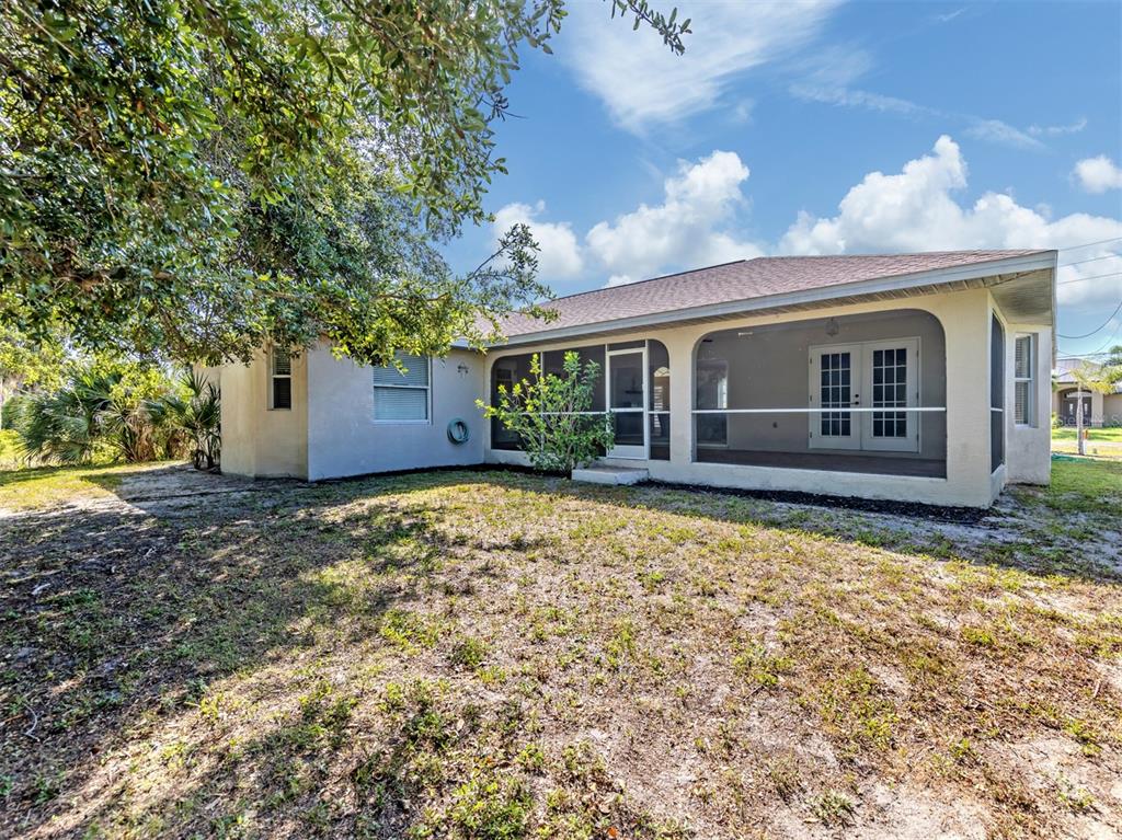 The exterior of a house features a screened-in back porch and a grassy yard — 1056 ROTONDA CIRCLE, ROTONDA WEST, FL