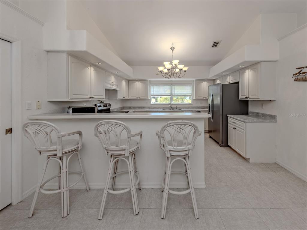 A kitchen features white cabinetry, a breakfast bar with three stools, and stainless steel appliances — 1056 ROTONDA CIRCLE, ROTONDA WEST, FL