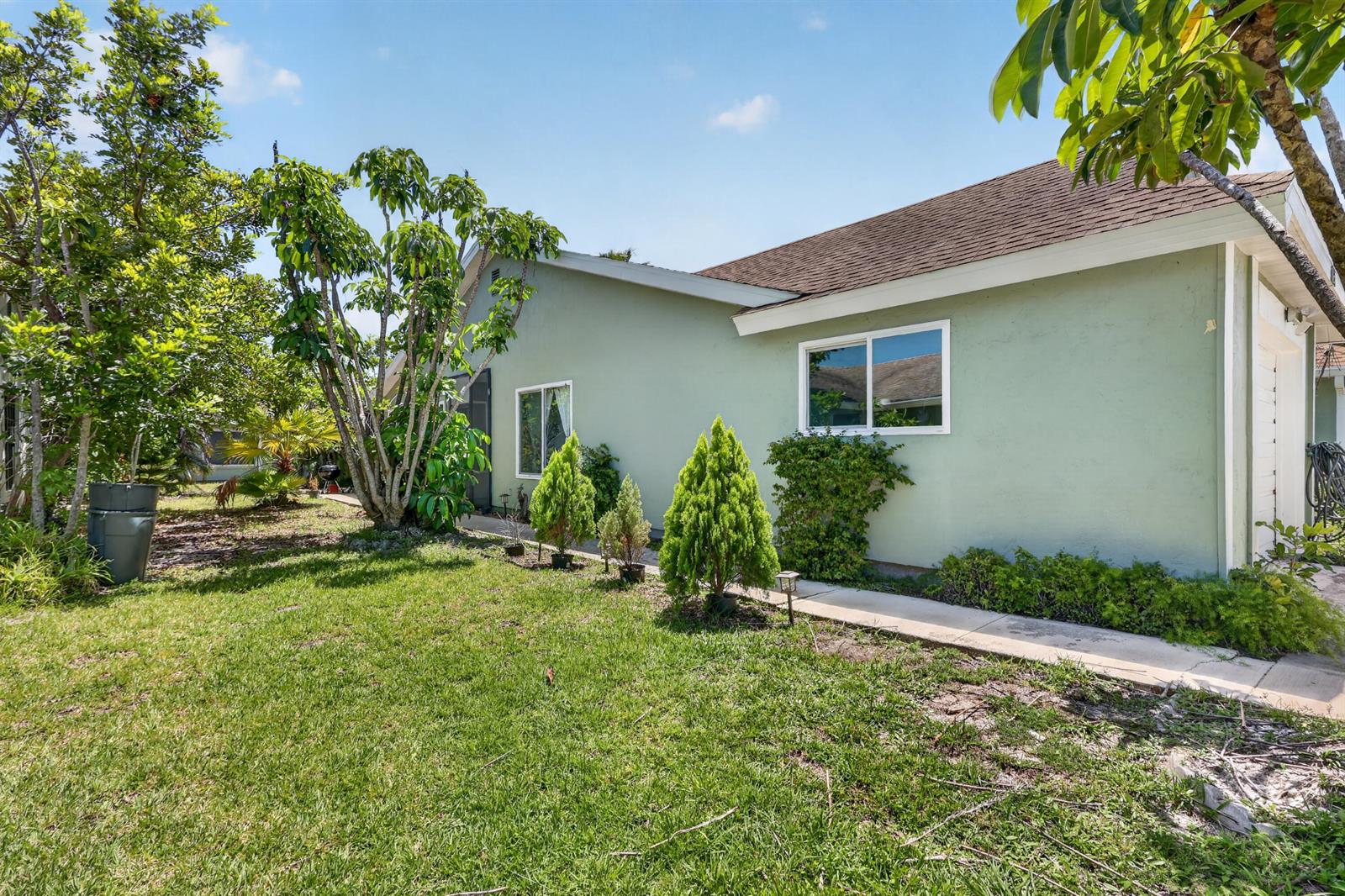 A light green house exterior with a lawn, small evergreen trees, and a concrete walkway — 1434 SE Larkwood Circle, FL 34952, FL