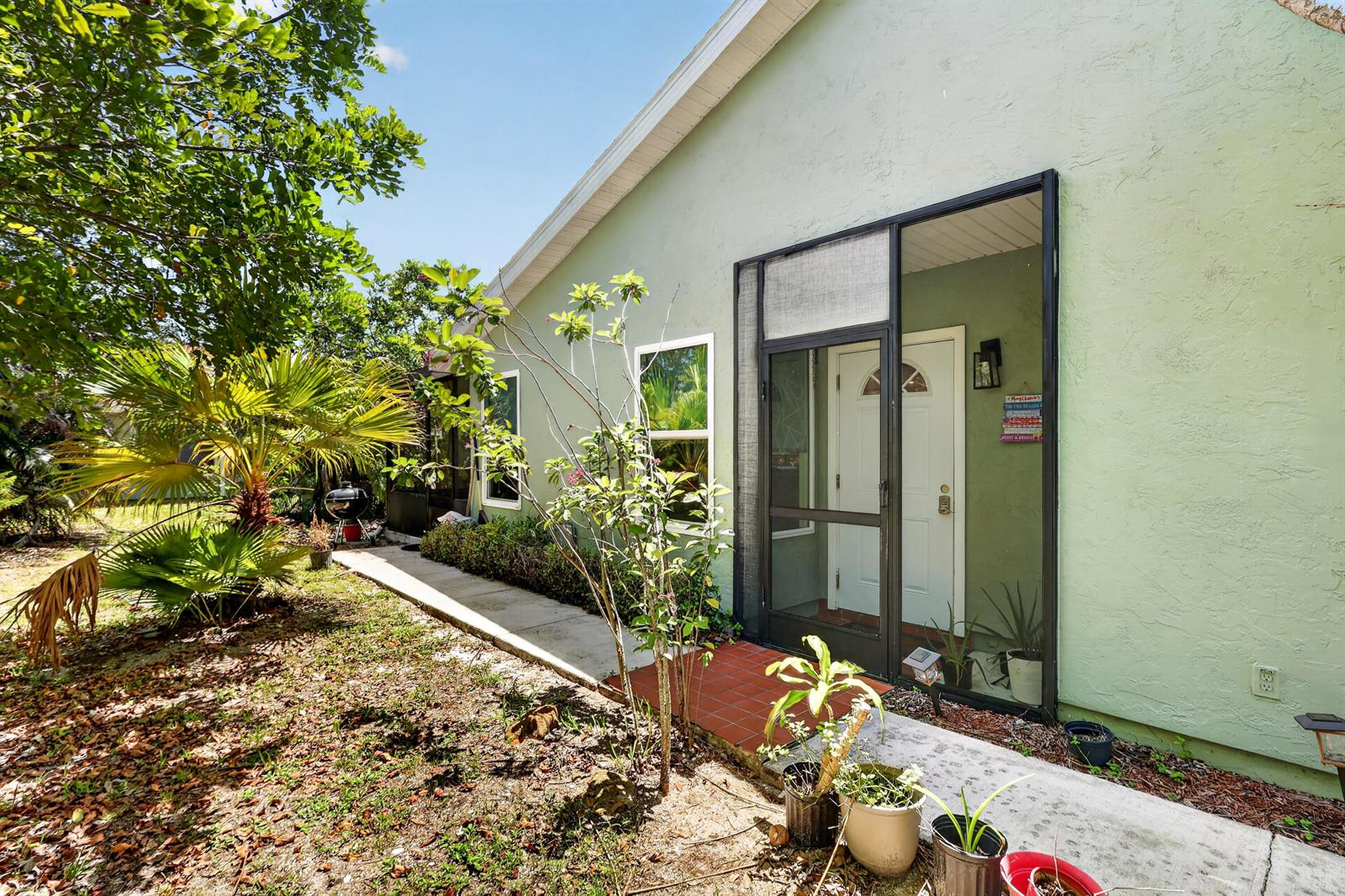 A light green house exterior features a screened front entryway with a white door — 1434 SE Larkwood Circle, FL 34952, FL
