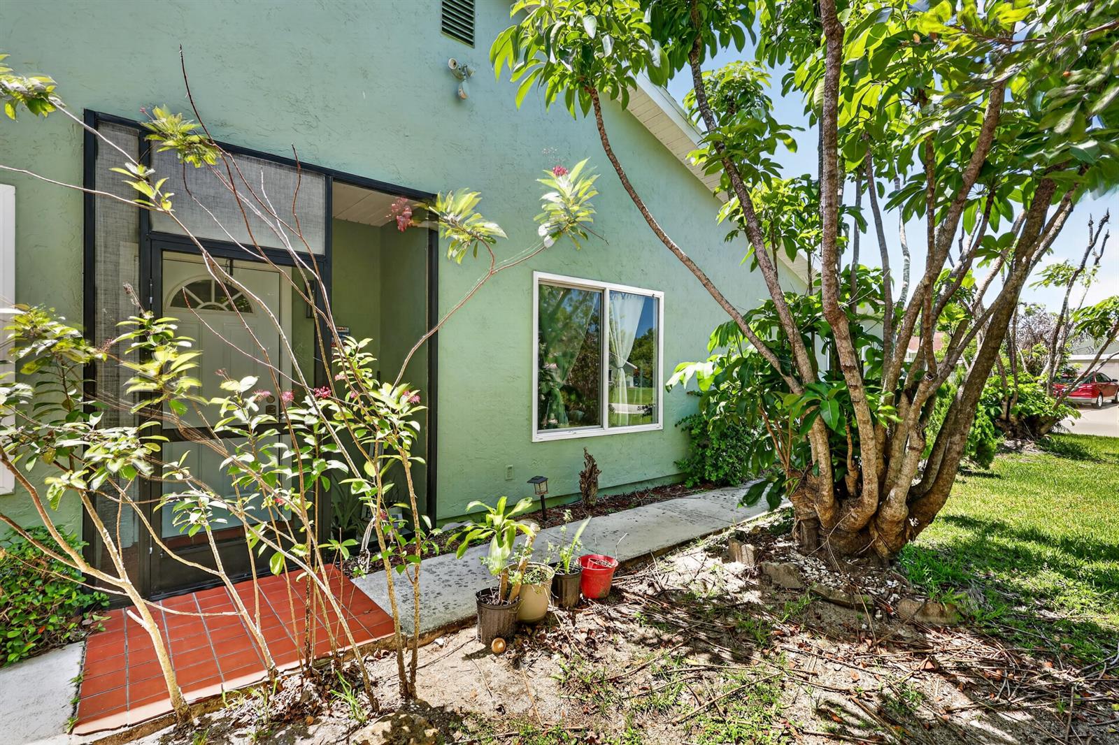 A green house exterior features a screened entryway, a window, and a large tree — 1434 SE Larkwood Circle, FL 34952, FL