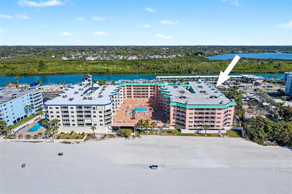 An aerial view of a multi-story beachfront condominium complex with a central pool area — 18400 GULF BOULEVARD UNIT 1302, INDIAN SHORES, FL