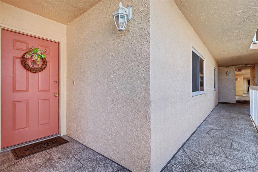 A pink front door with a wreath sits on a covered walkway with textured walls — 18400 GULF BOULEVARD UNIT 1302, INDIAN SHORES, FL