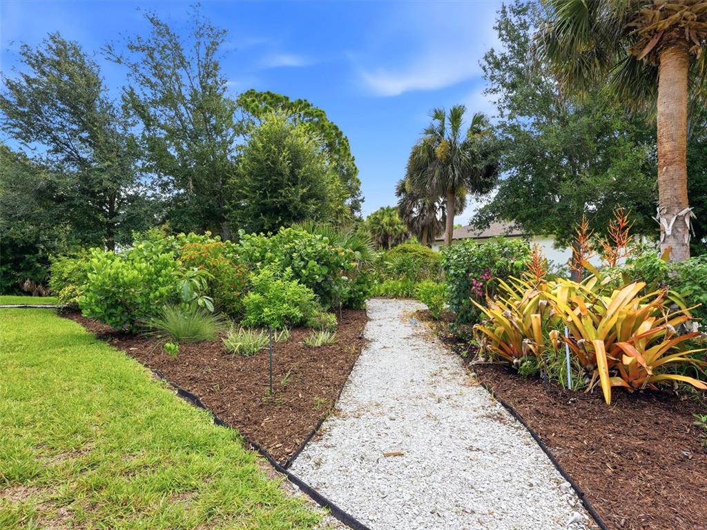 A gravel path winds through a landscaped garden with tropical plants, palm trees, and mulch — 162 MEDALIST ROAD, ROTONDA WEST, FL
