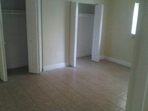 An empty room with tan tile flooring, two open closets, and a window — NORTH MIAMI BEACH, FL