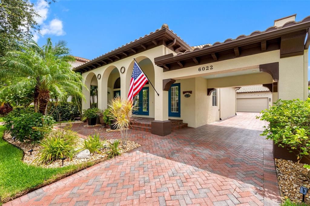A single-story house with a brick driveway, arched entryway, and a prominent American flag — 6022 BEACON SHORES STREET, TAMPA, FL