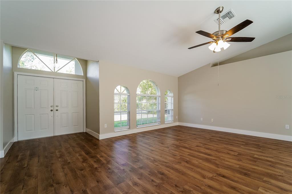 A living room with wood-look flooring, a vaulted ceiling, a ceiling fan, and arched windows — 1743 HAZELTON AVENUE, NORTH PORT, FL