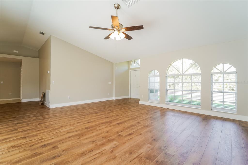 An empty living room features wood-look flooring, vaulted ceilings, a ceiling fan, and arched windows — 1743 HAZELTON AVENUE, NORTH PORT, FL