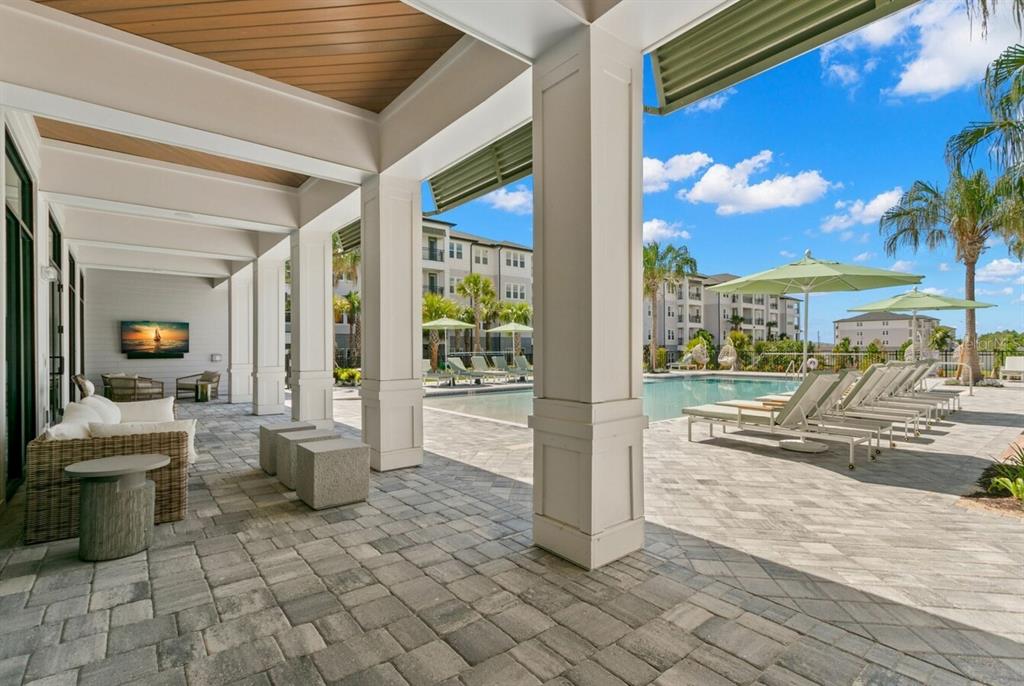 A covered patio with stone pavers overlooks a swimming pool with lounge chairs and umbrellas — 1310 RIDGEVIEW CIRCLE UNIT B1, DAVENPORT, FL