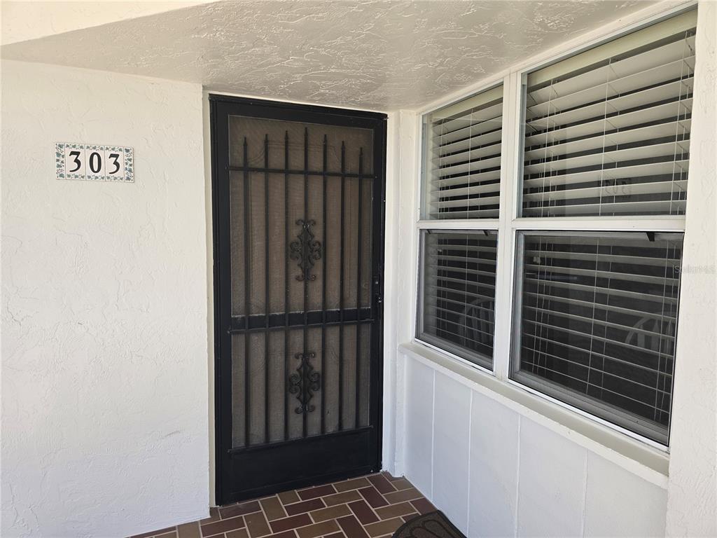 A white exterior entryway features a black metal security door and a window with blinds — 450 GULF OF MEXICO DRIVE UNIT 303, LONGBOAT KEY, FL