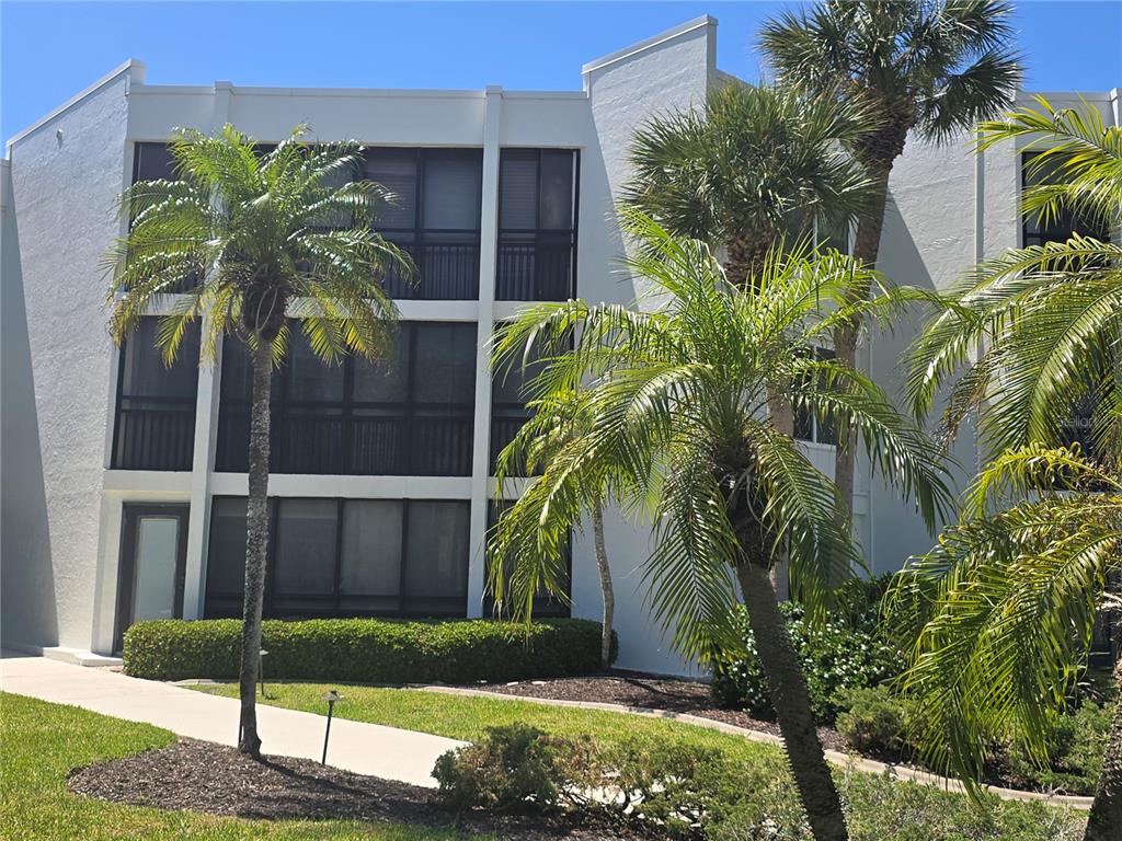 A three-story white apartment building with screened balconies and palm trees in the foreground — 450 GULF OF MEXICO DRIVE UNIT 303, LONGBOAT KEY, FL