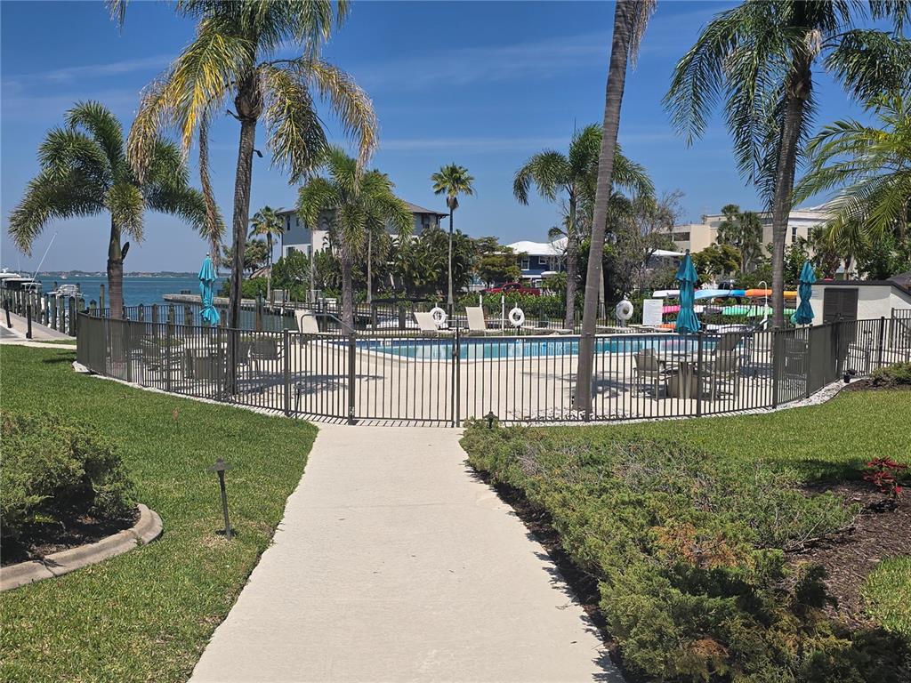 A fenced swimming pool area features palm trees, lounge chairs, and a view of water — 450 GULF OF MEXICO DRIVE UNIT 303, LONGBOAT KEY, FL