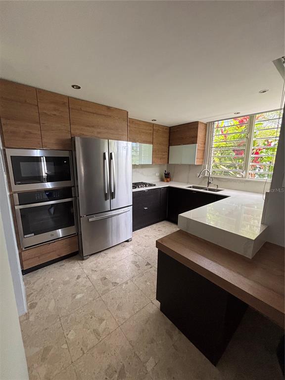 A modern kitchen features wood-tone cabinets, stainless steel appliances, and a white countertop peninsula — Calle 3 PASEO LAS VISTAS, SAN JUAN, PR