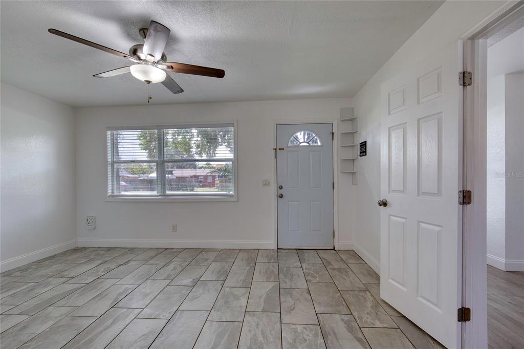 An empty room features white walls, light-colored tile flooring, a ceiling fan, and a front door — 843 NILES STREET, DAYTONA BEACH, FL