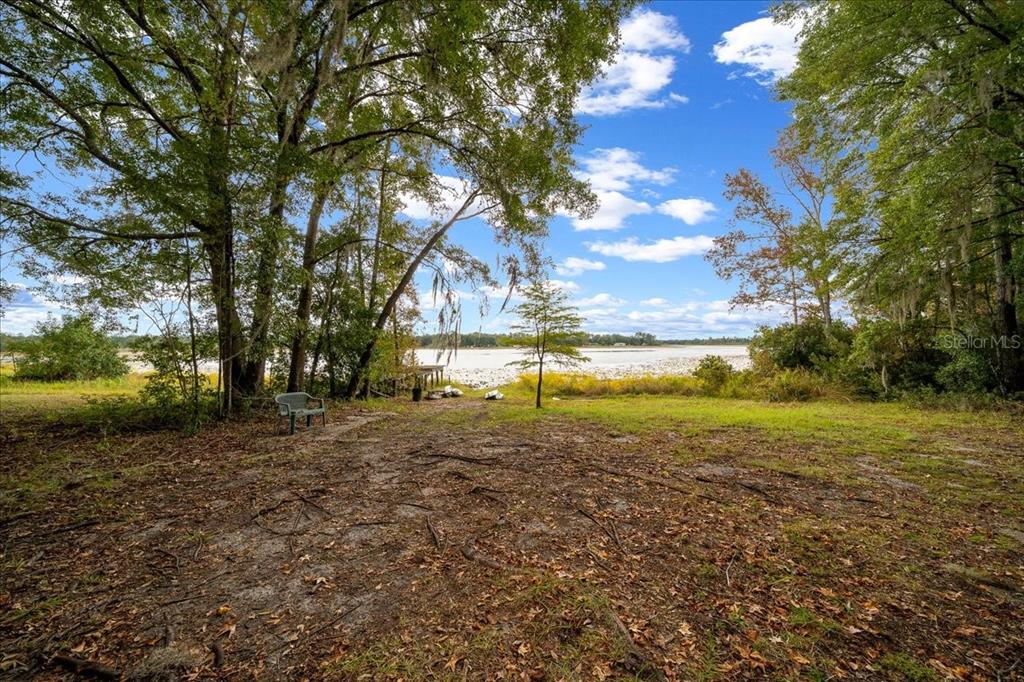 A grassy clearing leads to a lakefront view framed by large, moss-draped trees — 7173 W R THOMAS ROAD, KEYSTONE HEIGHTS, FL