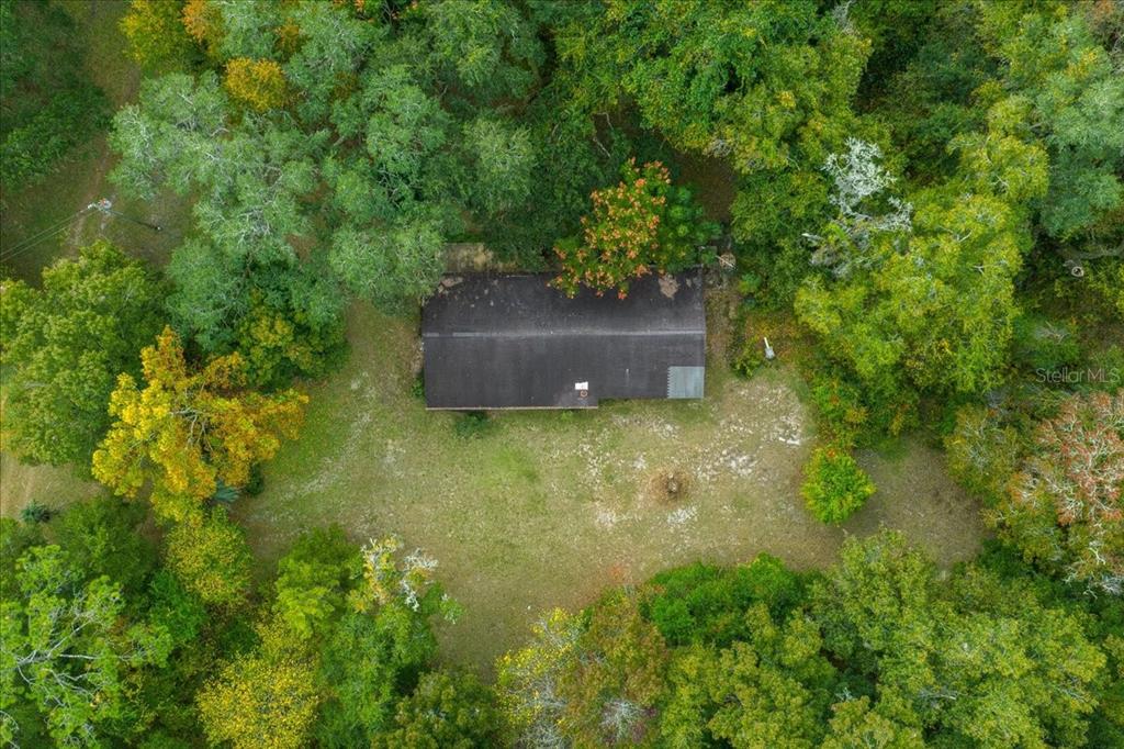 An aerial view shows a rectangular house with a dark roof surrounded by dense trees — 7173 W R THOMAS ROAD, KEYSTONE HEIGHTS, FL