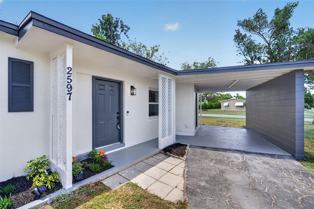 A single-story house exterior features a gray front door, a carport, and decorative lattice columns — 2597 STARLITE LANE, PORT CHARLOTTE, FL