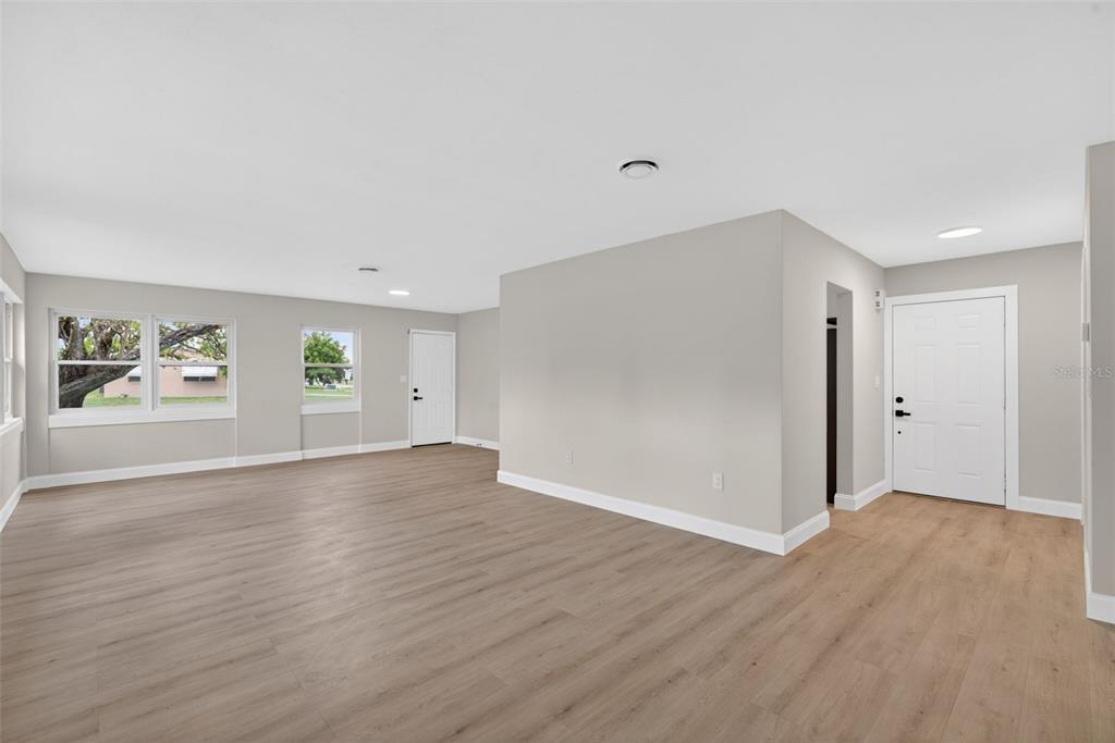 An empty living room with light gray walls, wood-look flooring, and a white front door — 2597 STARLITE LANE, PORT CHARLOTTE, FL
