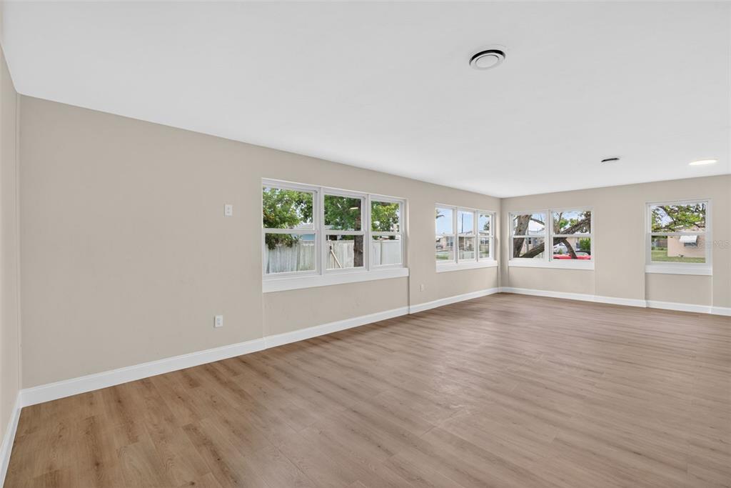 An empty room with light wood-look flooring, beige walls, and several windows — 2597 STARLITE LANE, PORT CHARLOTTE, FL