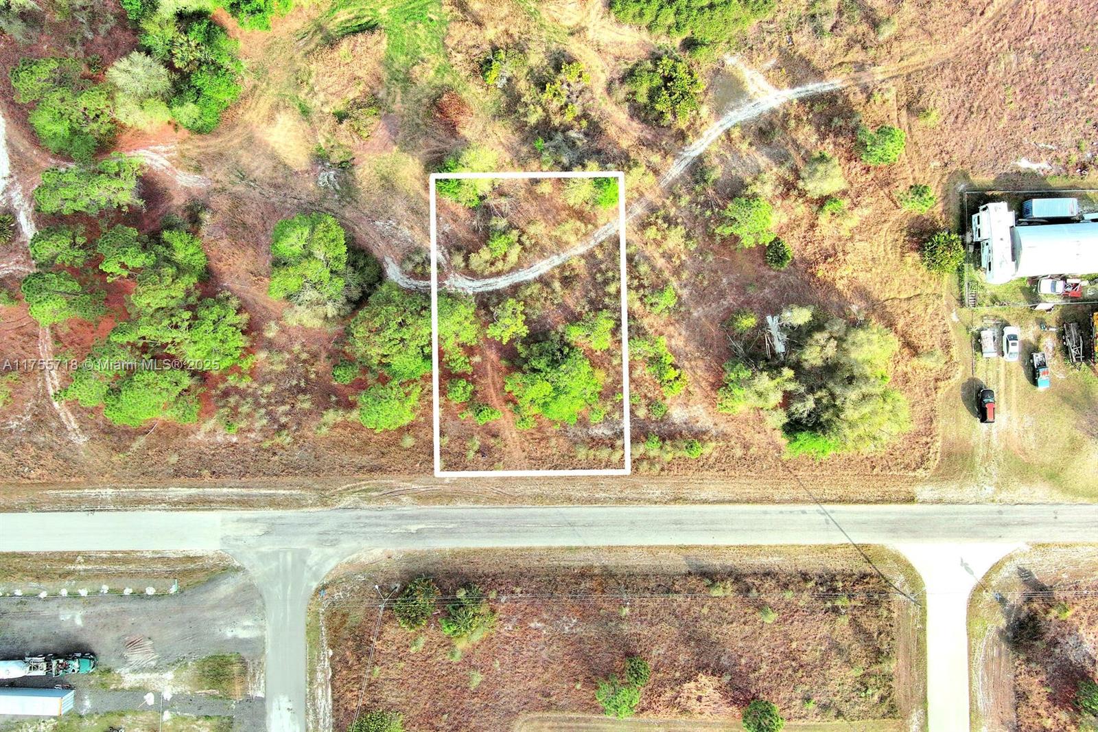 An aerial view shows a rectangular plot of land outlined in white near a road — 565 Summit Ave S, Lehigh Acres FL 33974, LEHIGH ACRES, FL
