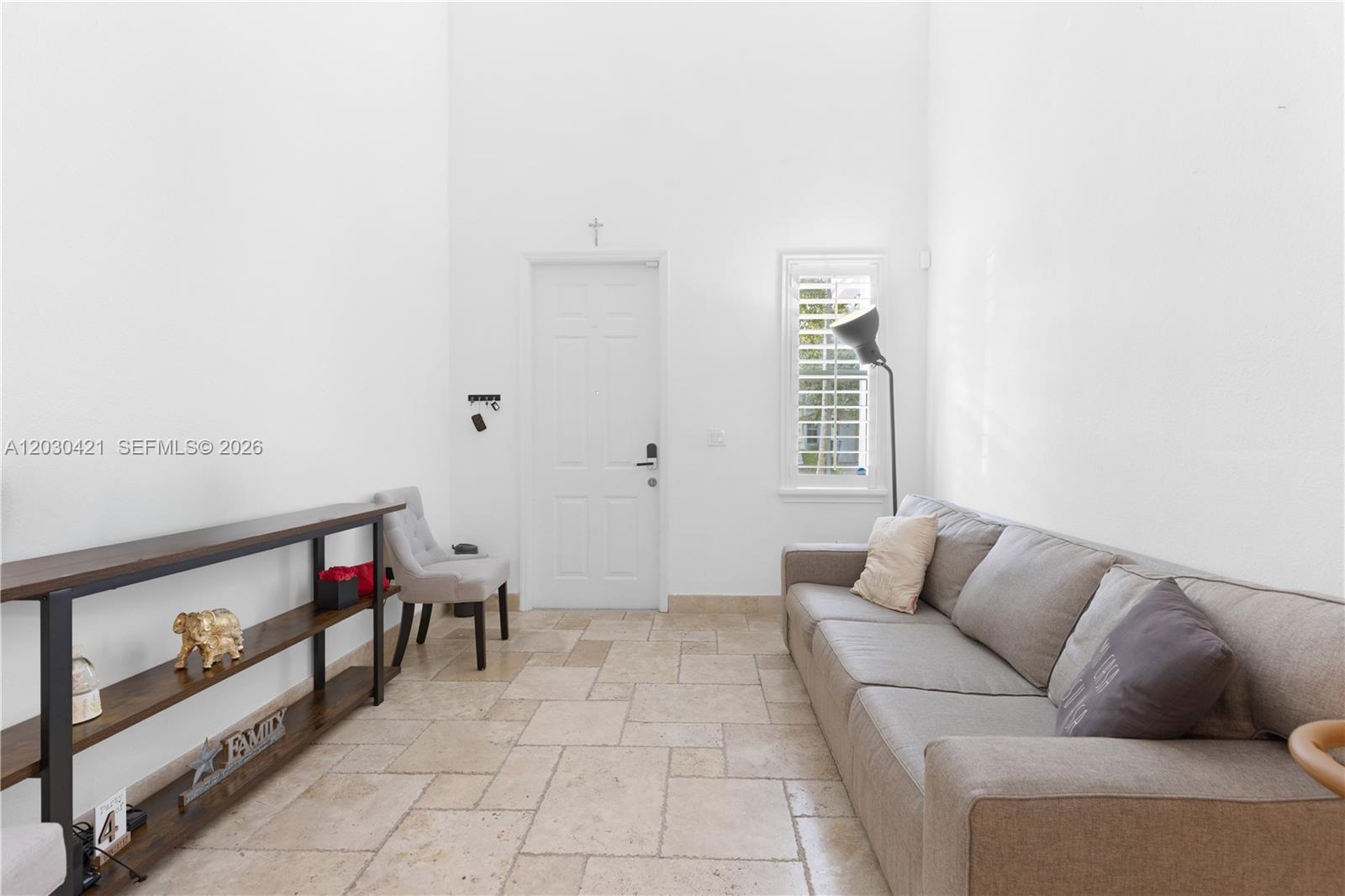 A living room features white walls, tile flooring, a grey sofa, and a wooden console table — 7475 NW 116th Ave, Doral FL 33178, DORAL, FL