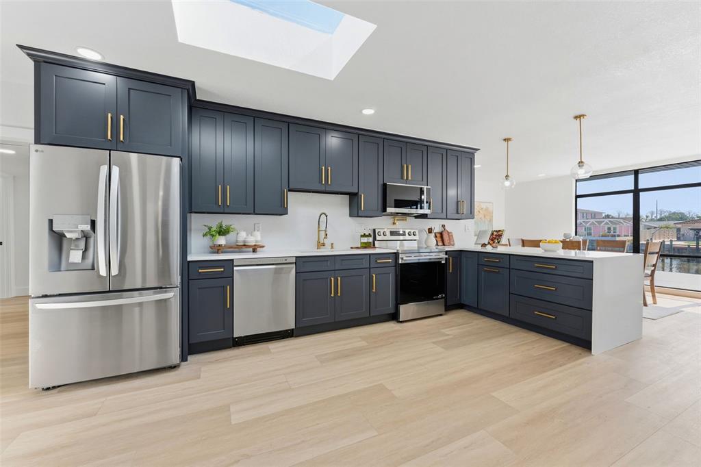 A modern kitchen features dark blue cabinetry, stainless steel appliances, and light wood flooring — 3917 E EDEN ROC CIRCLE, TAMPA, FL