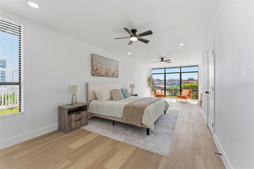 A bedroom features light wood flooring, a bed with neutral bedding, and large floor-to-ceiling windows — 3917 E EDEN ROC CIRCLE, TAMPA, FL